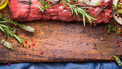 Raw roast beef  with herbs and spices tied with a rope on wooden background, top view, border
