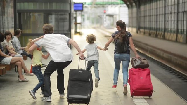 Young family of two spouses, son and daughter, running in the railway station, father holding daughter, parents and children traveling and be late