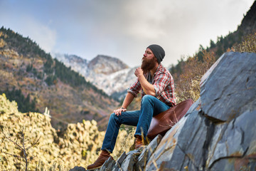 contemplative bearded man with luggage on top of mountain relaxing