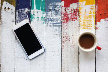 smartphone and coffee cup on grunge colorful wooden panels as ba