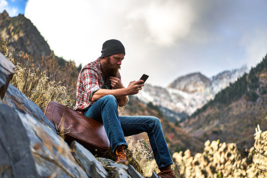 hipster vagabond using smart phone out in the mountains