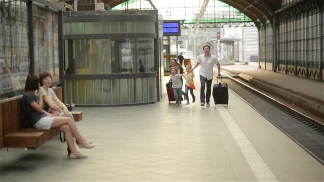 Young family of two spouses, son and daughter, running to catch the train before it leaves the railway station without them, parents and children traveling and be late