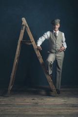 Vintage 1920s man in suit standing on old wooden ladder in empty