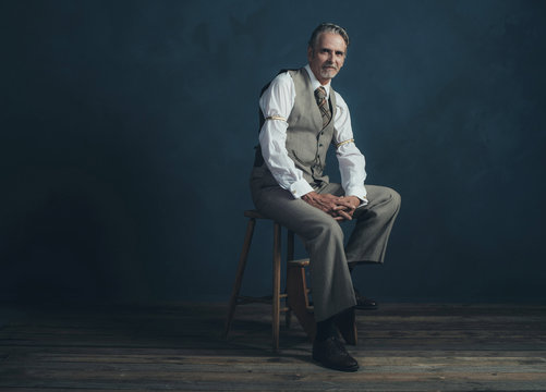 Confident Retro 1920s Fashion Man Sitting On Wooden Chair In Emp