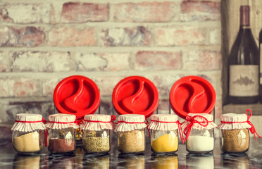 Spices in glass jars with beautiful covers, tied with red thread on dark table in the kitchen