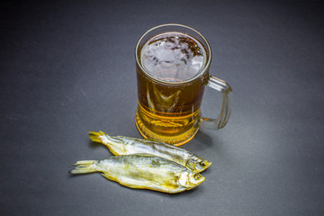 Beer and dried fish snack on black background.