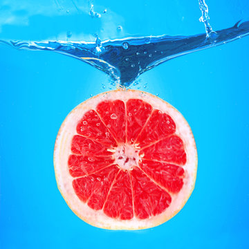 Fresh grapefruit falling in water on blue background © Africa Studio