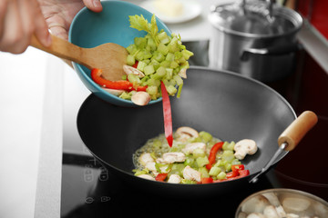 Female hands putting vegetables into pan closeup