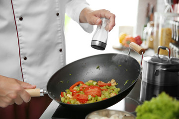 Female hands putting salt to vegetables in pan closeup