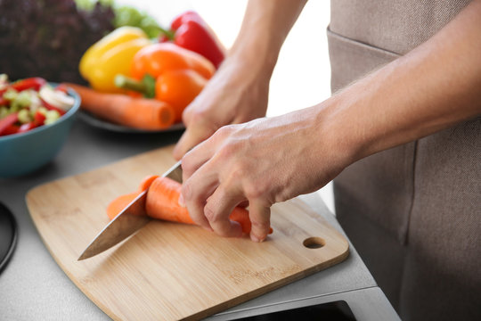 Male hands cutting carrot on wooden board closeup
