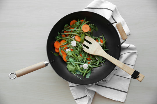 Vegetables and wooden spatula in pan  on wooden table, top view