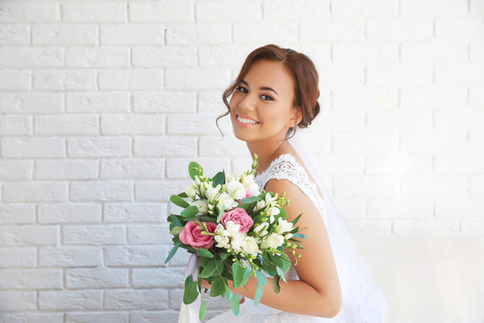 Beautiful bride with wedding bouquet on white brick wall background