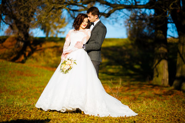 Fototapeta premium Newlyweds kissing and smiling on their wedding day on the walk outdoors. Funny bride with bouquet of flowers.