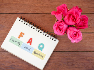 word spell FAQ and pink rose flower on wood background 1