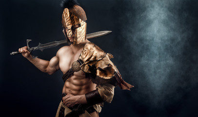 Portrait of handsome muscular gladiator with sword. Isolated. Studio shot. Black background