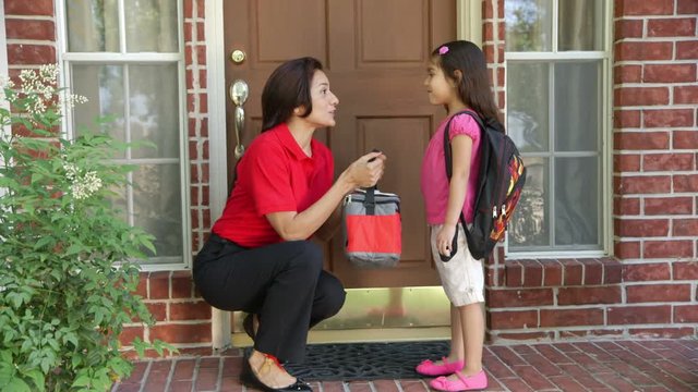 A little Hispanic girl wearing a backpack gives her mother a little kiss after getting her lunch bag and a cheerful send off to school.