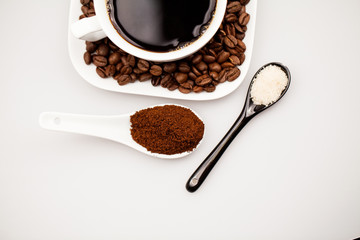 White coffee cup with coffee, plate with coffee beans and black teaspoon with brown sugar