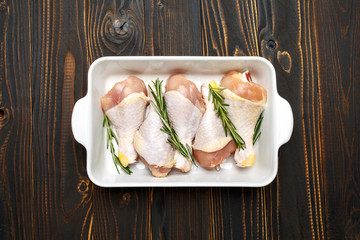 Raw chicken legs in baking dish on a wooden background