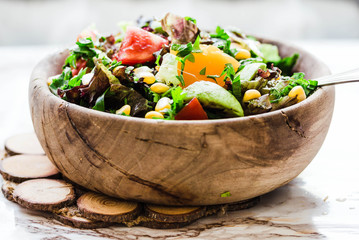 fresh green salad with avocado and corn in wooden plate