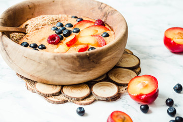 smoothie bowl with peaches, plums and blueberries in a wooden di