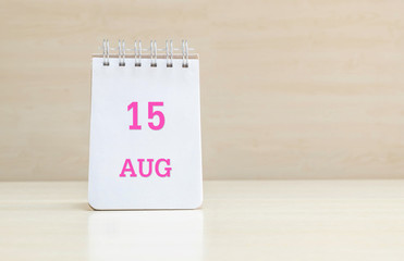 Closeup surface note book with pink 15 aug word  in page on blurred brown wood desk and wood wall textured background with copy space under window light