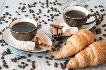 Cup of coffee with grains, croissant, turkish delight and cinnamon sticks on wooden background