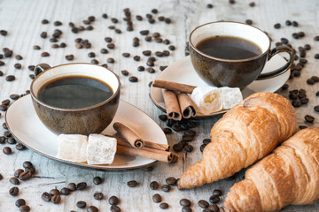Cup of coffee with grains, croissant, turkish delight and cinnamon sticks on wooden background