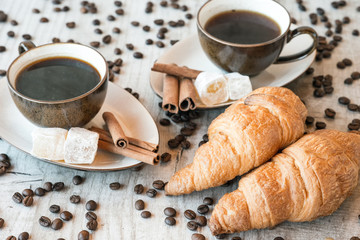 Cup of coffee with grains, croissant, turkish delight and cinnamon sticks on wooden background