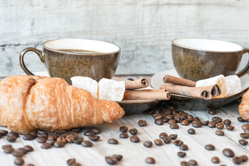 Cup of coffee with grains, croissant, turkish delight and cinnamon sticks on wooden background