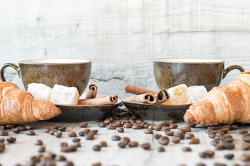 Cup of coffee with grains, croissant, turkish delight and cinnamon sticks on wooden background