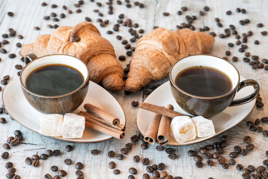 Cup of coffee with grains, croissant, turkish delight and cinnamon sticks on wooden background