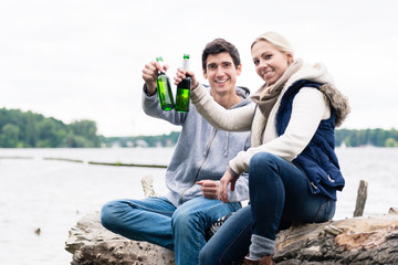 couple sitting on tree stump at the riverside drinking beer