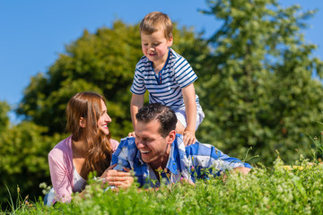 Familie liegt im Gras auf der Weise, der Sohn reitet auf Papa