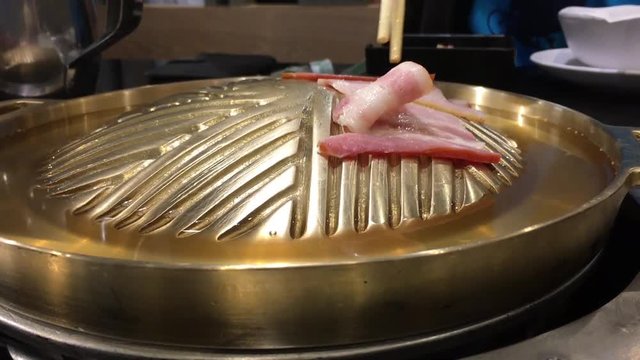 Korean meat and beacon grilled style on hot gold stove with smoke and boiled water closeup and eating with chopsticks which is popular in East Asian Culture