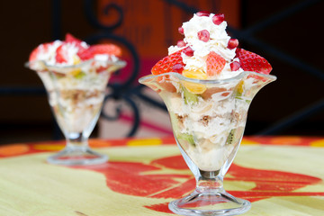 Fresh fruits salad with milky cream in glass bowl and fruits on wooden table