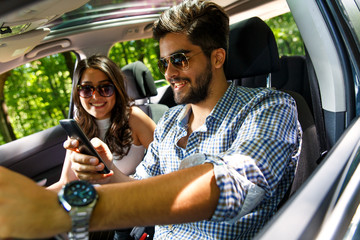 Portrait of young couple driving a car. He is looking at mobile phone. 