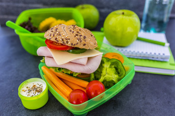 Tasty food in plastic lunch box with school supplies on dark background.
