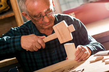 Senior carpenter working in his workshop. He is using a hammer.