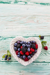 Forest fruits in a bowl in the shape of a heart on a wooden table with space for text.