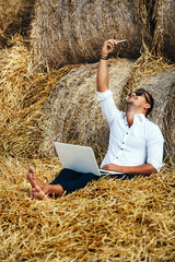 Naklejka na ściany i meble Business man looks beautiful works with a laptop and talking on the phone sitting in haystack.