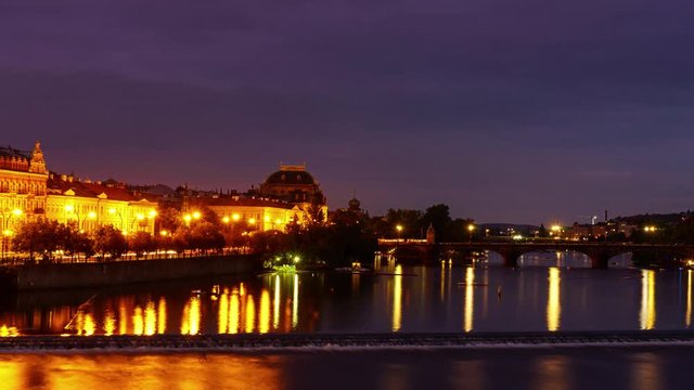 4k time-lapse video of Vltava river and Prague National Theatre with bridge and light trails from cars during summer August night with street lights and very cloudy sky. Reflection of city in River.