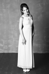 Fototapeta premium Portrait of a woman in an evening dress. Beautiful girl with make-up in full growth on a background of gray wall.