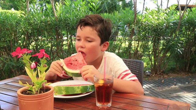 Preteen boy holding  and eating a piece of watermelon at the restaurant