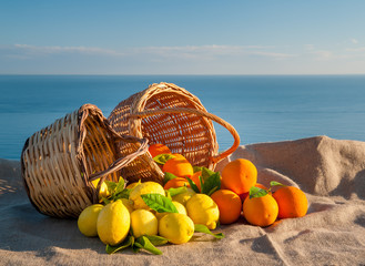Wicker baskets full of oranges and lemons on a piece of jute with blue sky and sea in the background