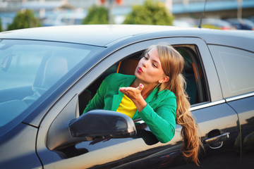 Fototapeta na wymiar Girl behind wheel of car sends air kiss