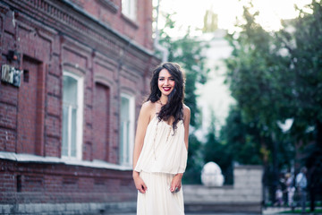 Beautiful girl on white dress walking on a warm sunny day in the city. Young brunette long-haired beautiful woman, lifestyle concept