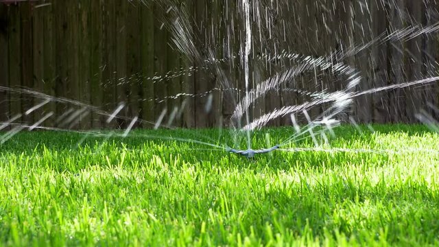 Water from a backyard sprinkler twirls and spins around in dance like fashion bathed in afternoon sunlight. Slow motion footage.