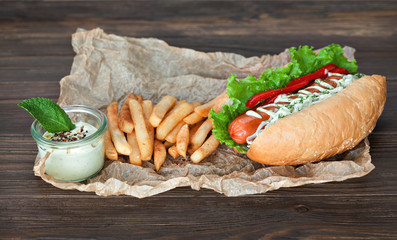 Big tasty hot dog with sausage and vegetables with sauce and French fries on the parchment on the...