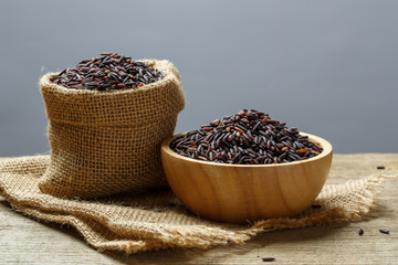 Rice berry or uncooked brown rice in bowl and burlap sack on woo