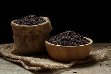 Rice berry or uncooked brown rice in bowl and burlap sack on woo